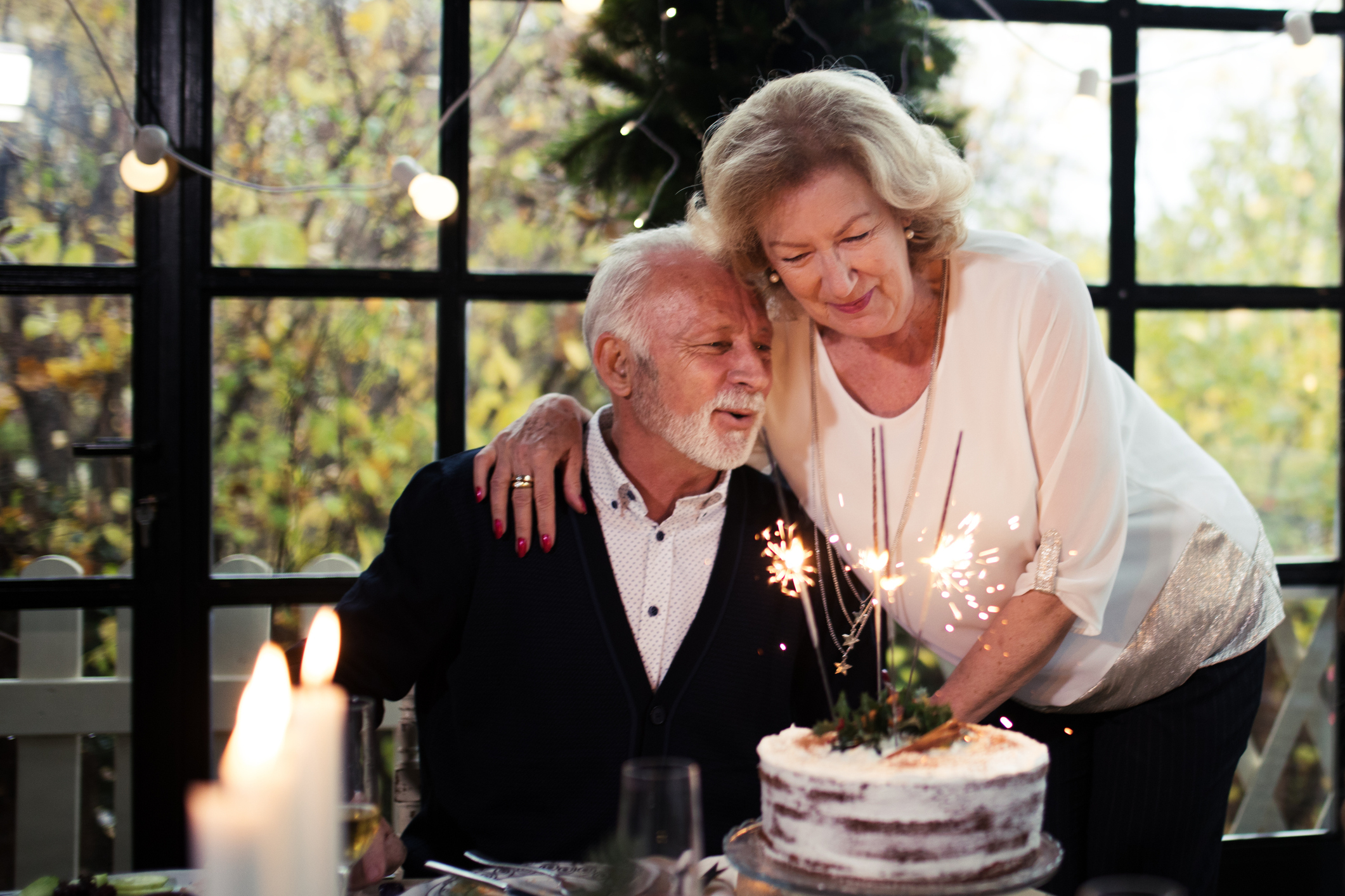 Older couple celebrating with a sparkler on a cake in an affectionate pose