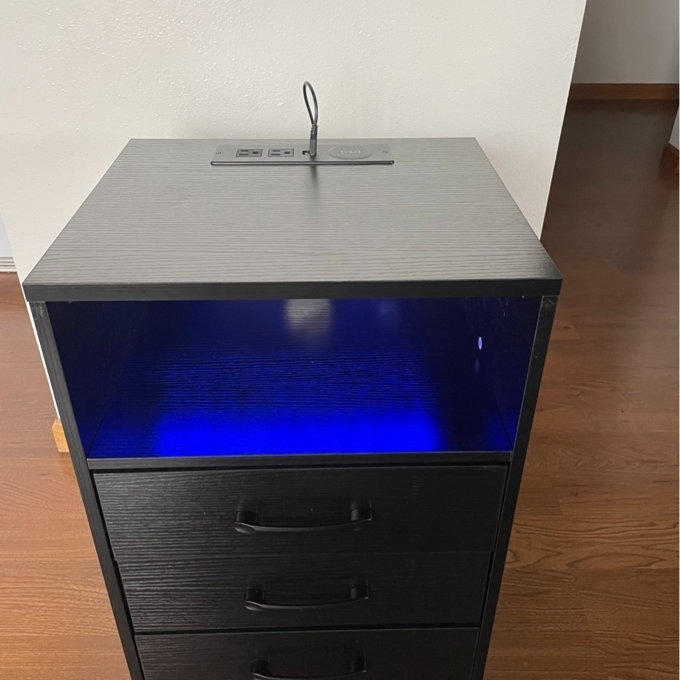 Black filing cabinet with a blue LED light inside, placed against a plain wall