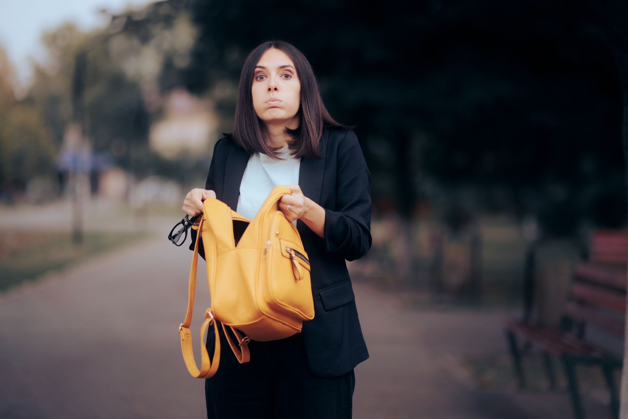 Woman in a blazer holding a yellow bag looking surprised on a street