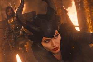 Maleficent with horns and a dark outfit, looking intently, with a figure in armor behind her