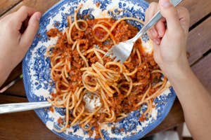 Person eating spaghetti bolognese with a fork from a patterned plate