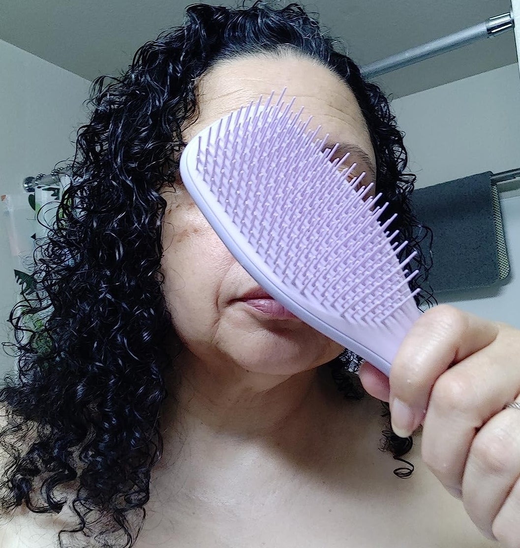 a reviewer holds a detangling brush over face with smooth curly hair
