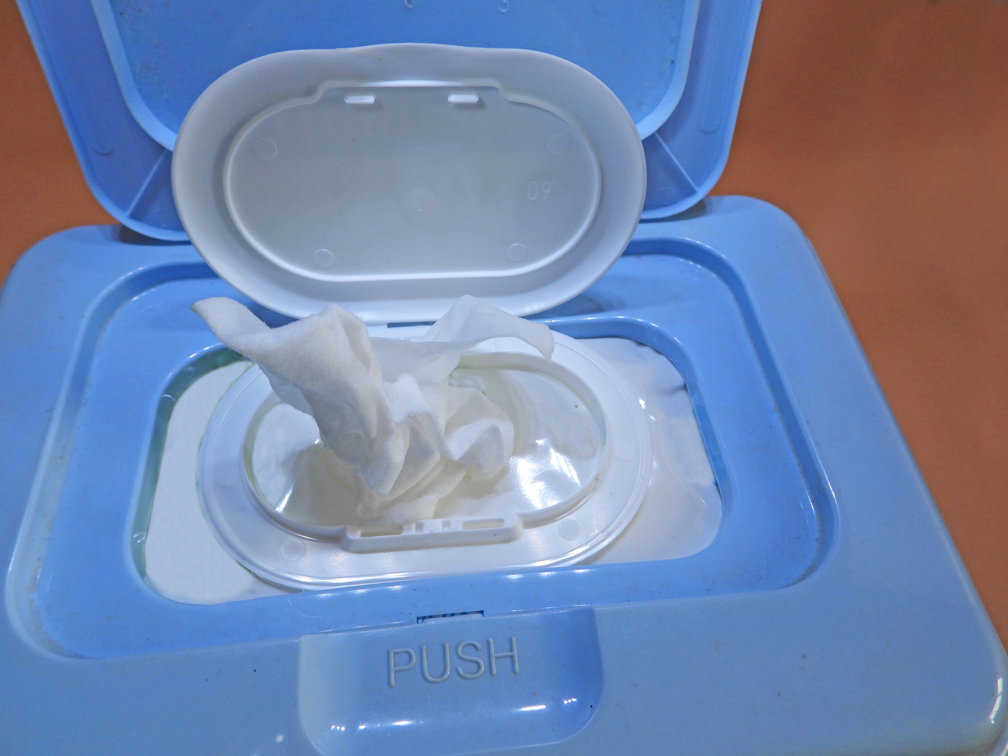 Wet wipe emerging from a plastic dispenser labeled &quot;PUSH,&quot; highlighting ease of use and accessibility