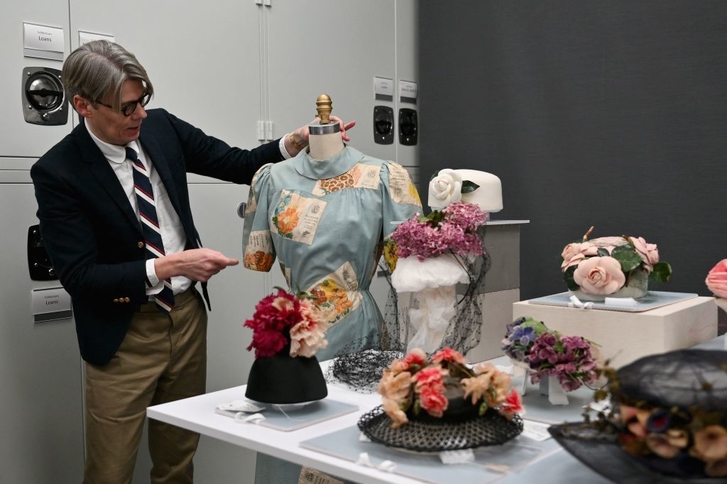 Andrew Bolton examining vintage-style mannequin heads with ornate hats and accessories