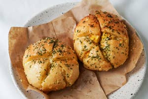 Two garlic bread knots on a plate with herbs sprinkled on top