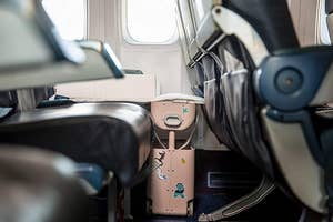 the suitcase in front of an airplane seat, with it raised up, creating a leg rest for kids to make the seat more comfortable