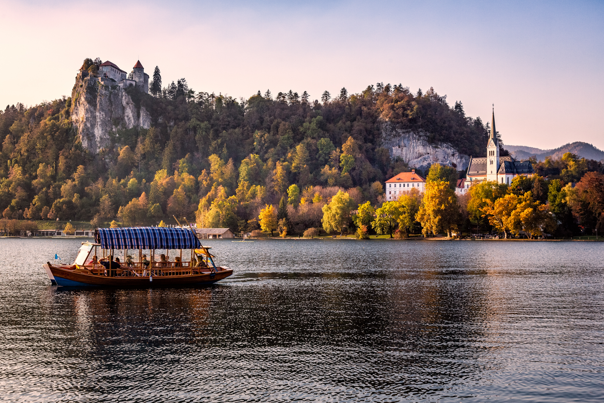 Traditional boat on a calm lake with a castle on a hill and a church spire in the background, conveying a serene travel scene