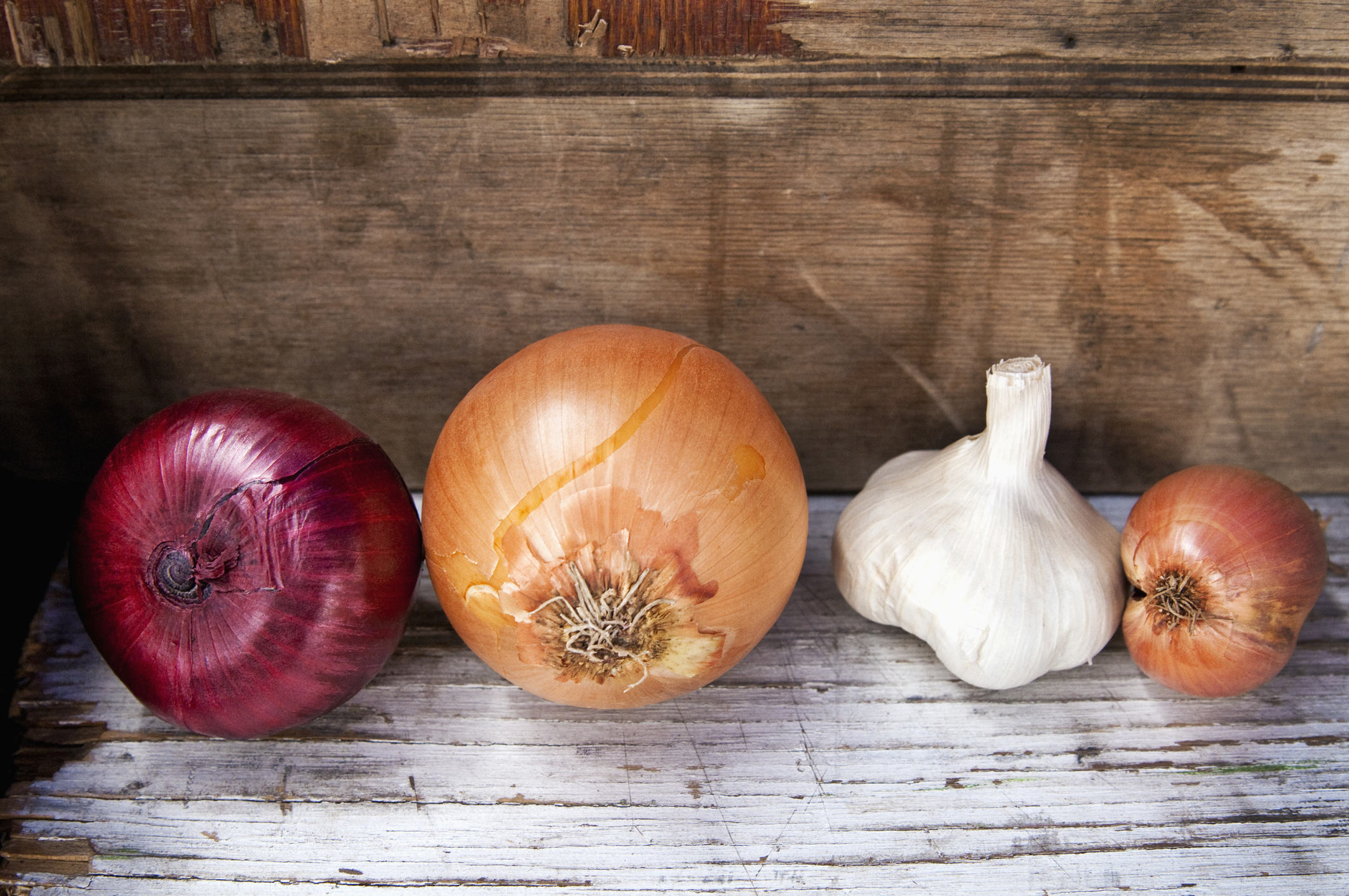 Red and gold onions with a bulb of garlic on a wooden surface.