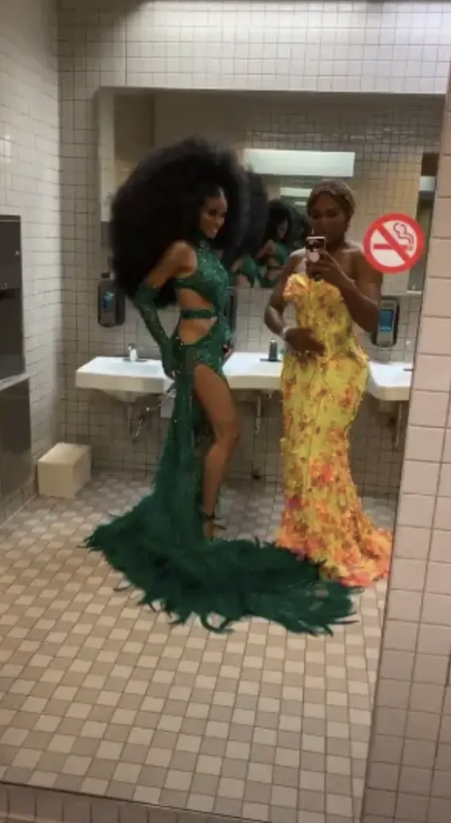 Ciara and Serena Williams in glamorous dresses posing for a mirror selfie in a restroom
