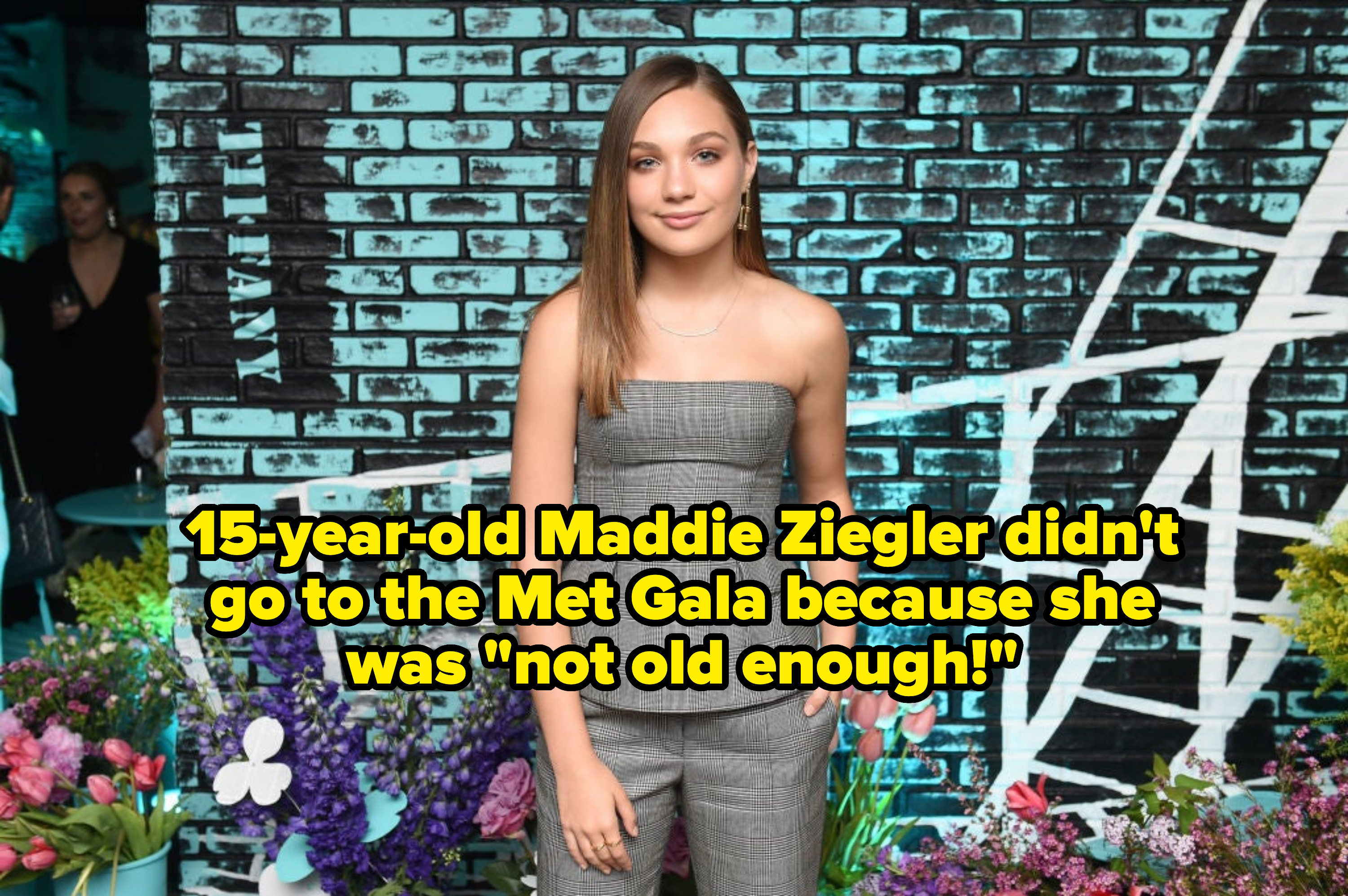 Maddie Ziegler standing before a floral and graffiti backdrop, wearing a strapless plaid ensemble