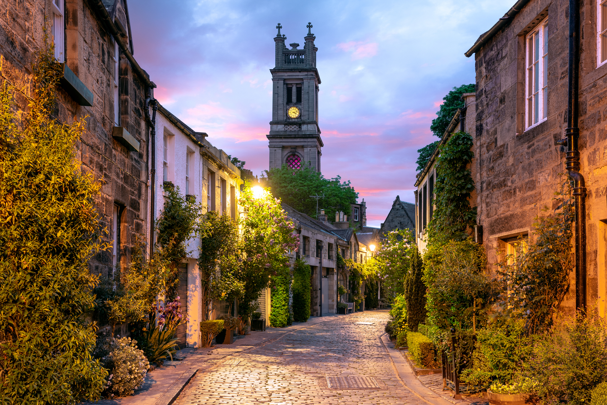 Cobbled street leads to a clock tower between old buildings at dusk