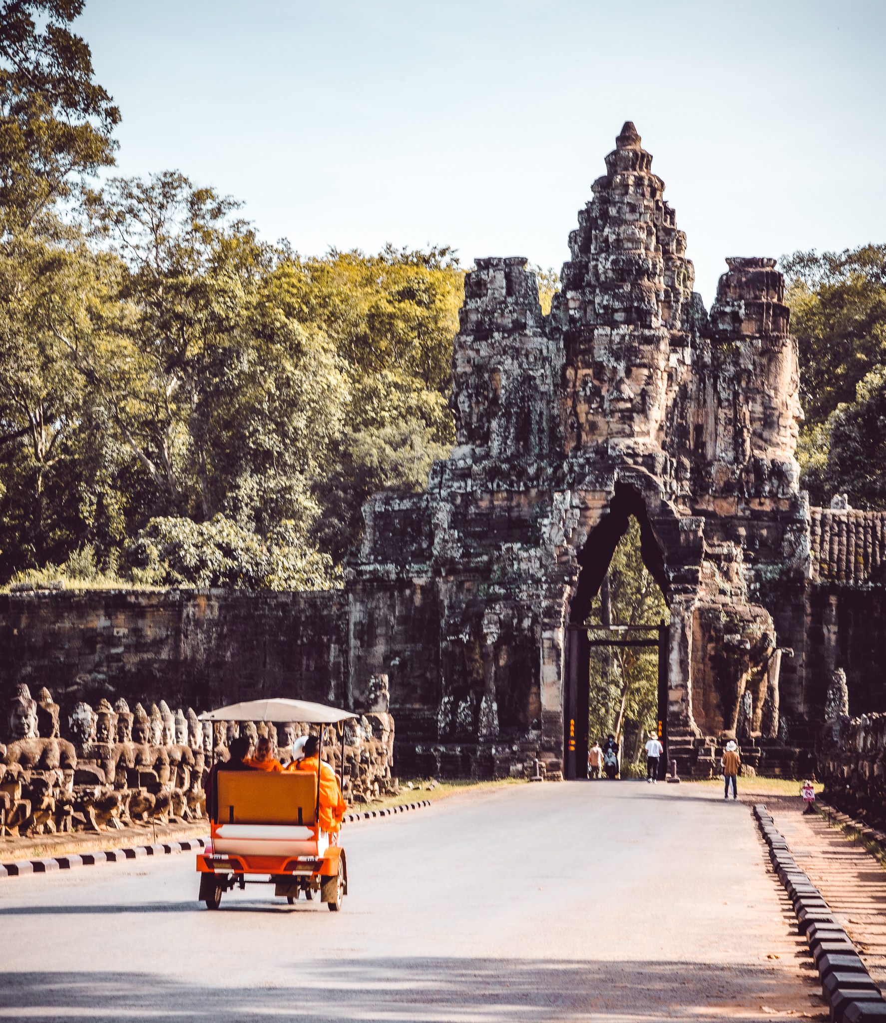 Tuk-tuk on a road approaching a historic stone gate with sculptures on the sides