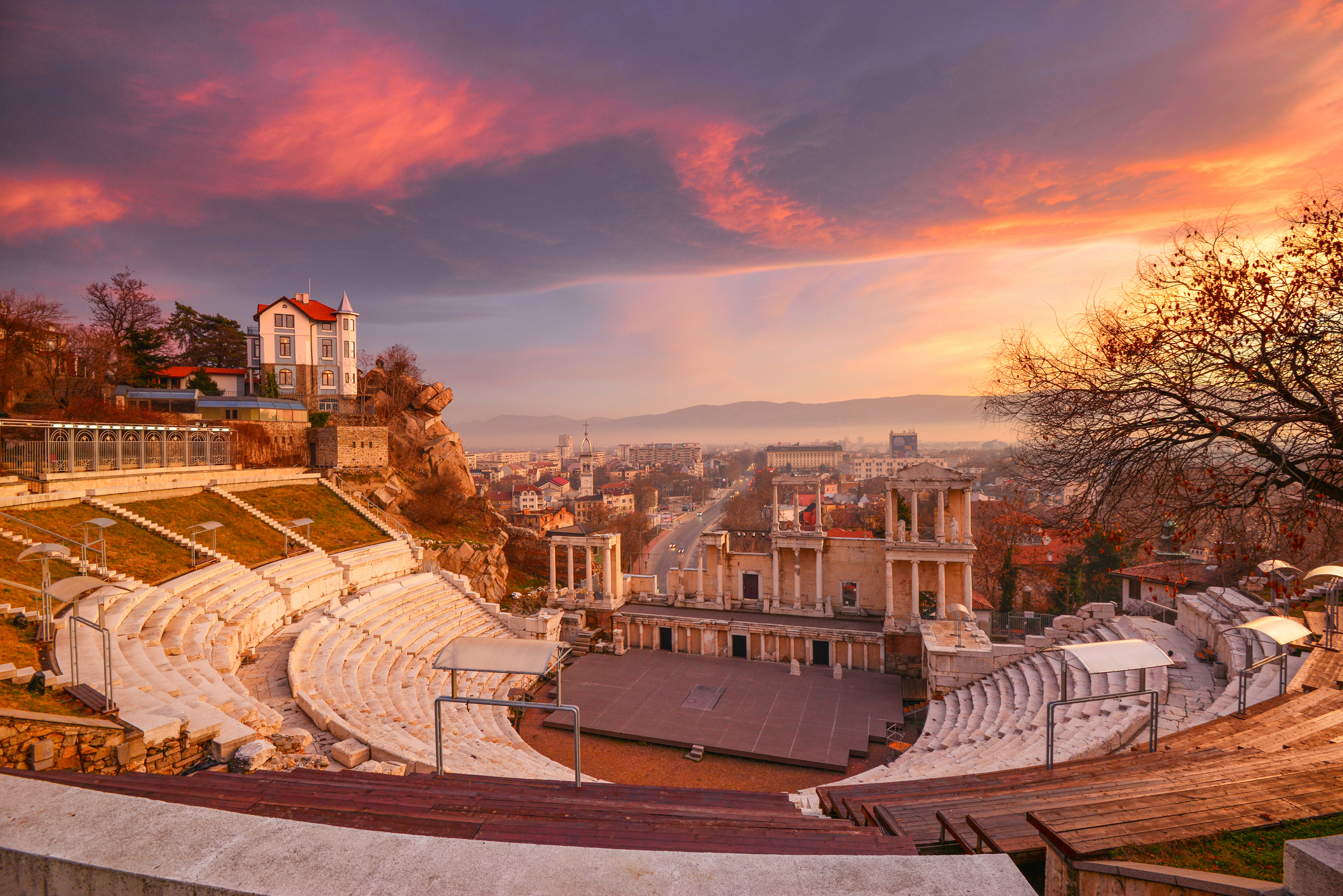 Sunset over an ancient outdoor amphitheater with cityscape and dramatic sky in the background
