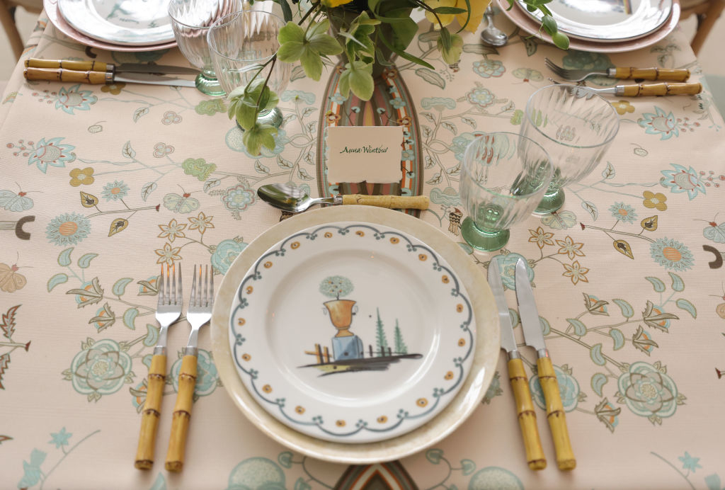 A table setting with a place card reading &quot;Anna Wintour,&quot; floral dishes, and bamboo-style flatware