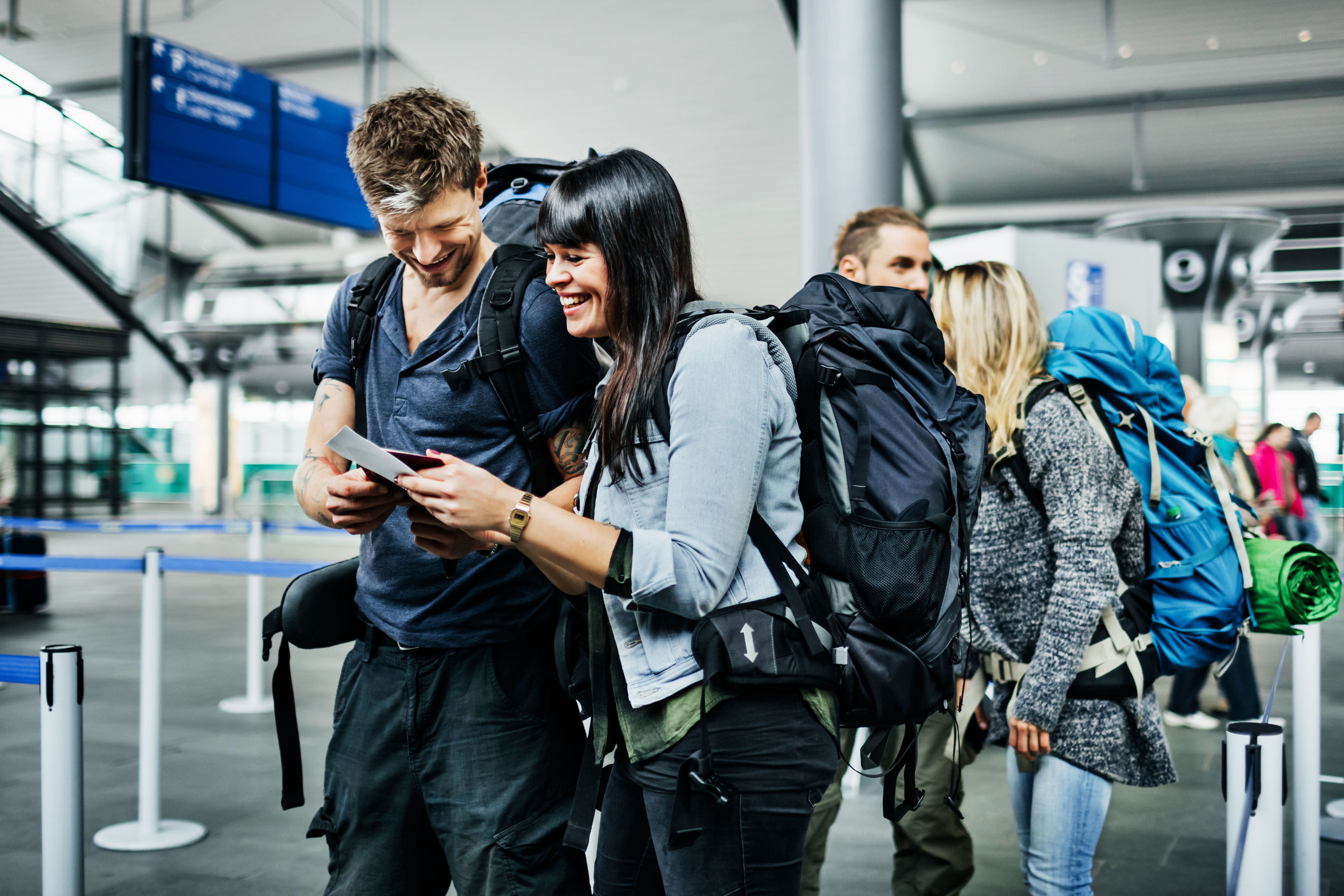 Two travelers with backpacks in an airport smiling at a smartphone