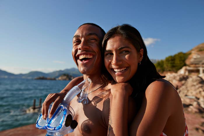 Two people smiling with a snorkel, embracing by the sea