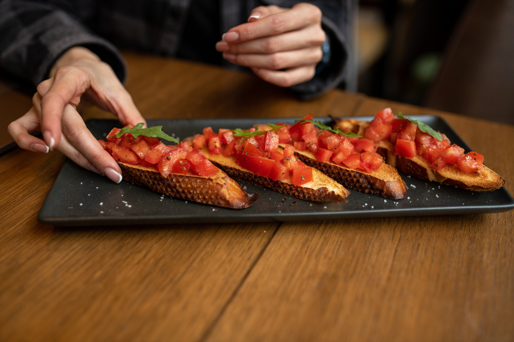 Person reaches for a slice of bruschetta on a platter, hands visible but not faces