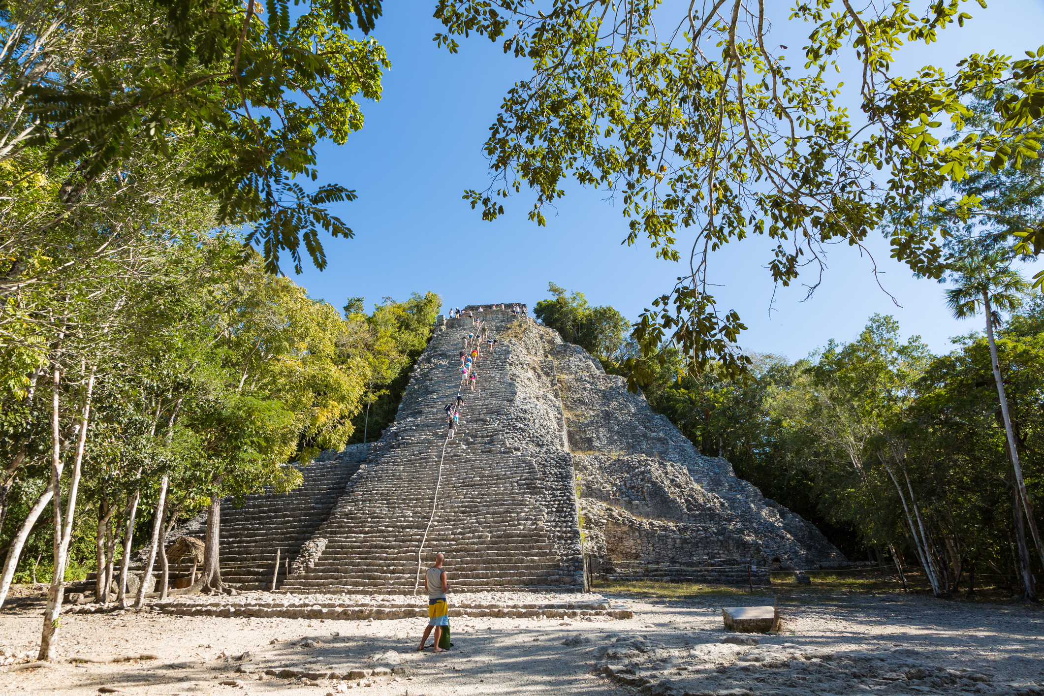 Ancient pyramid with visitors climbing and standing at the base amidst trees