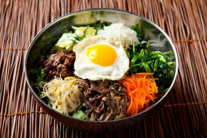 A bowl of bibimbap with an assortment of vegetables, beef, a fried egg, and rice