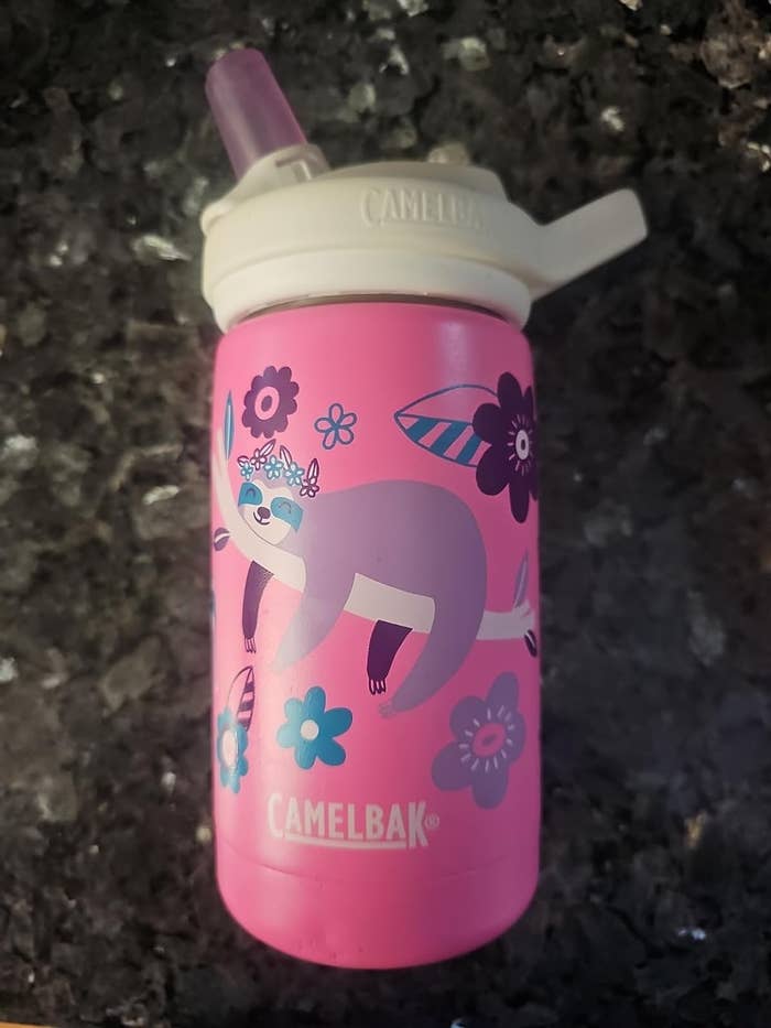 A pink CamelBak water bottle with a cute raccoon and flower design