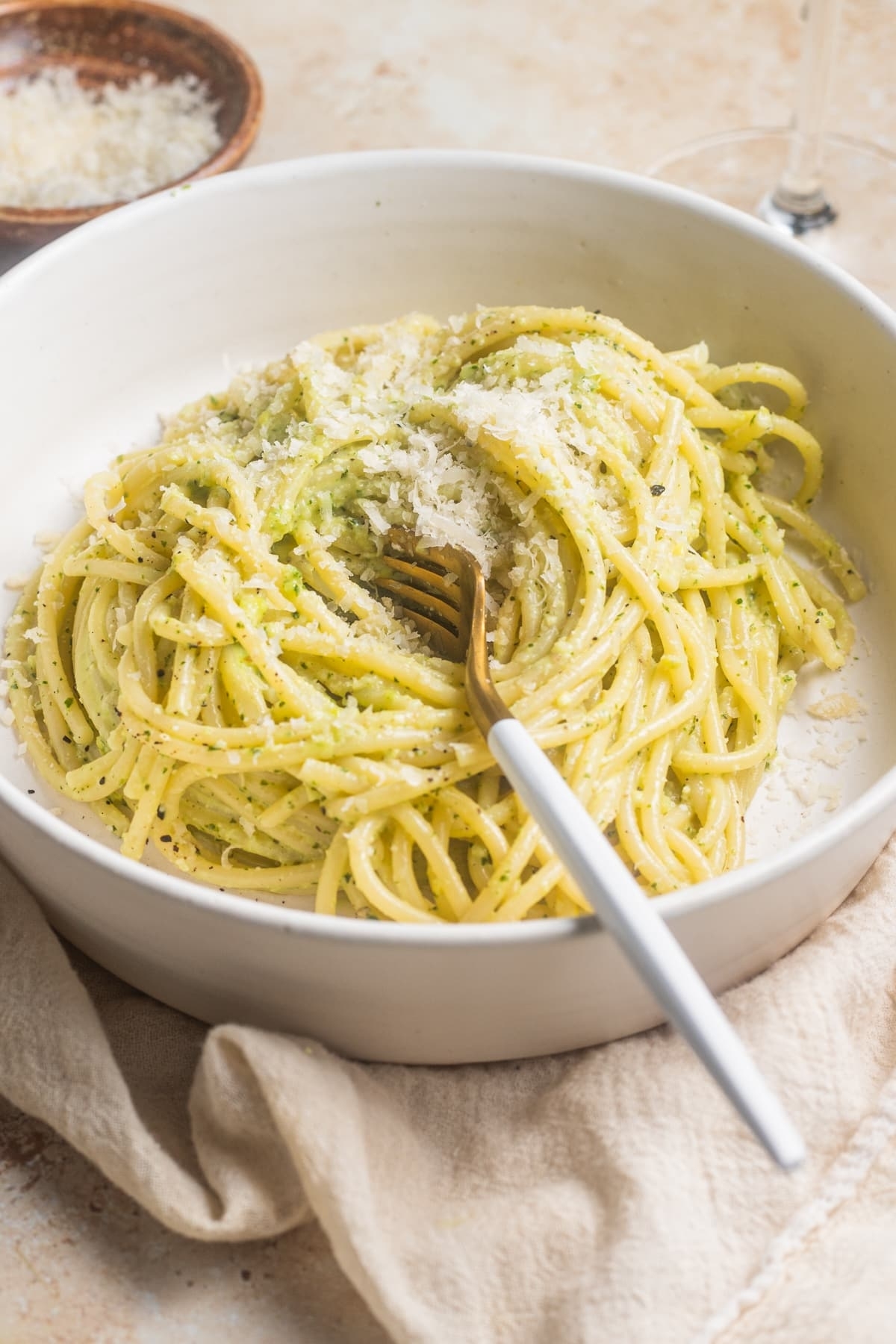 A bowl of spaghetti tossed in pesto sauce, garnished with grated cheese, with a fork