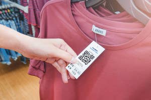 Person examining a clothing tag with a QR code, indicating price and brand information, in a store setting