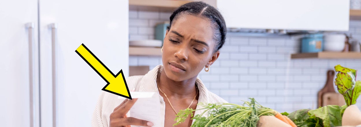 Woman frowning slightly while reading a label on a product next to grocery bags