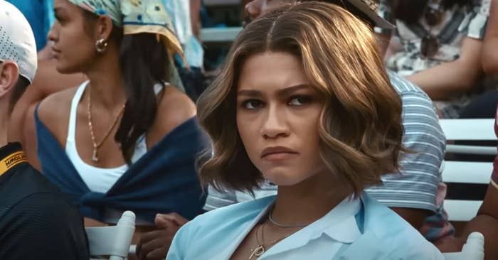 Zendaya in a light blouse with a pensive expression at an outdoor event