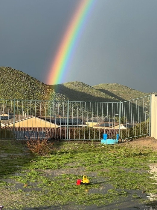 Rainbow arching over a terrain with a metal fence and scattered toys on ground
