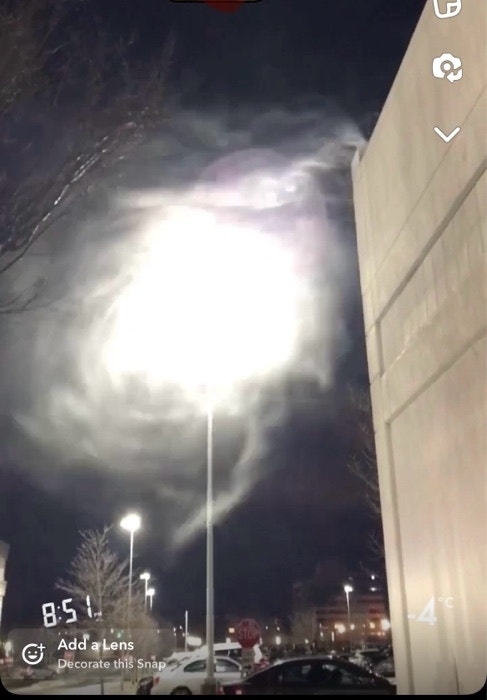 Bright light illuminates clouds at night, with Snapchat interface visible