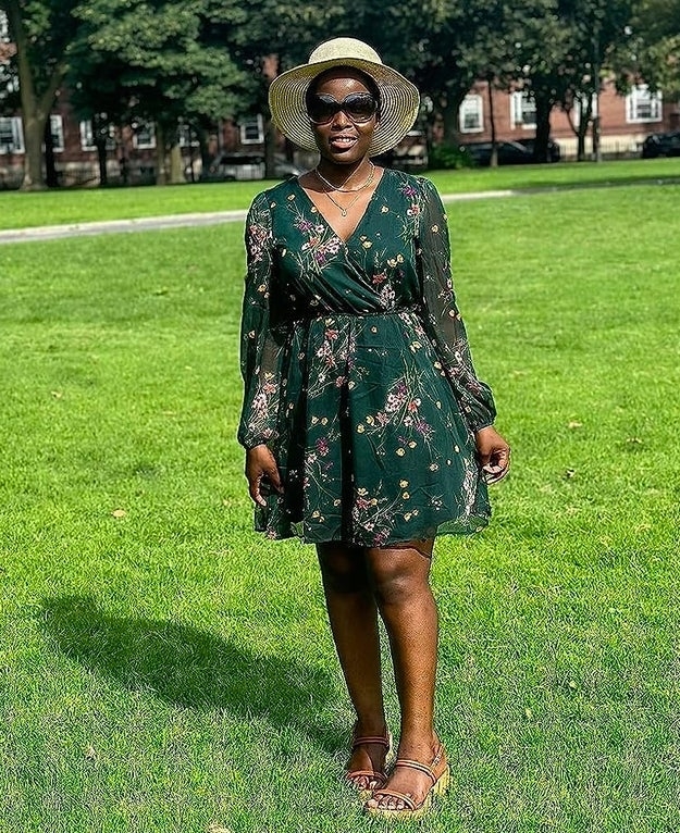 Woman in a floral wrap dress and sunhat stands on grass, potentially showcasing a summer outfit for shopping inspiration