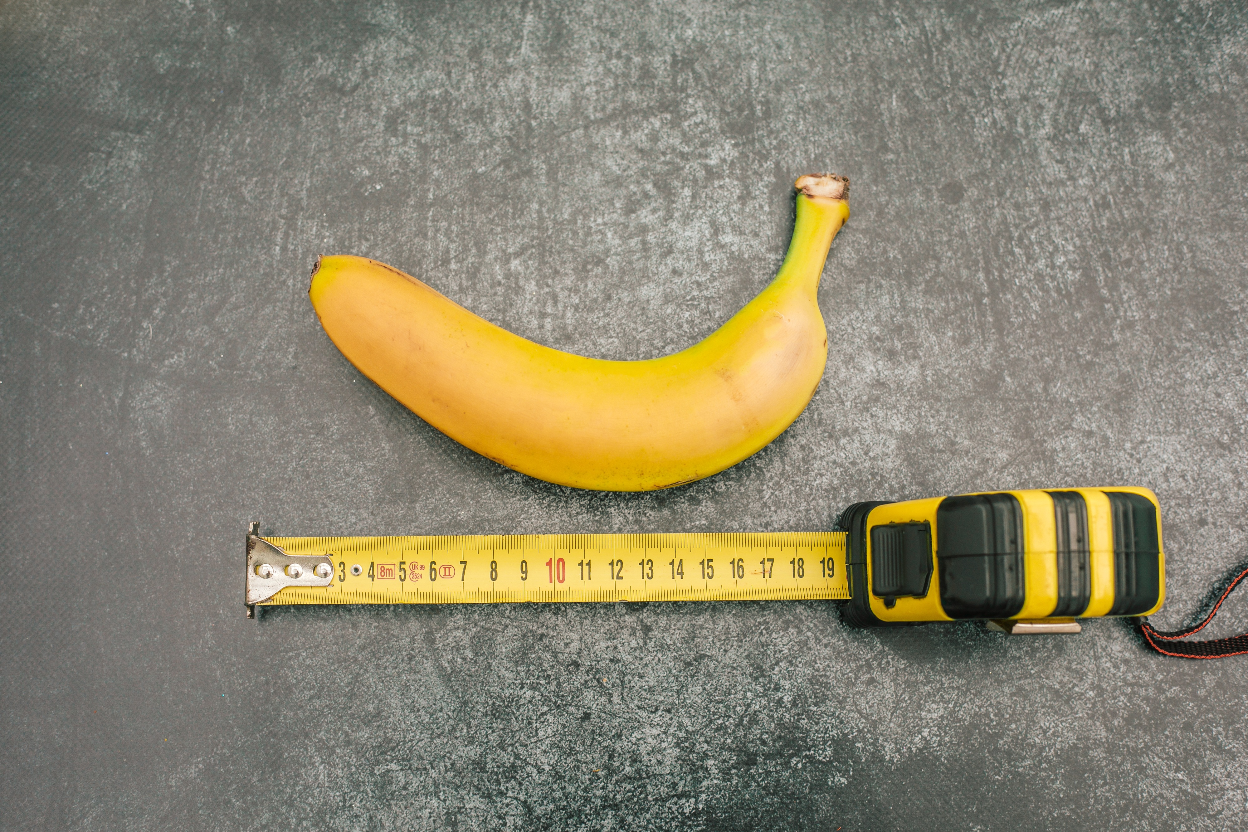 Banana next to a measuring tape showing length on a gray surface