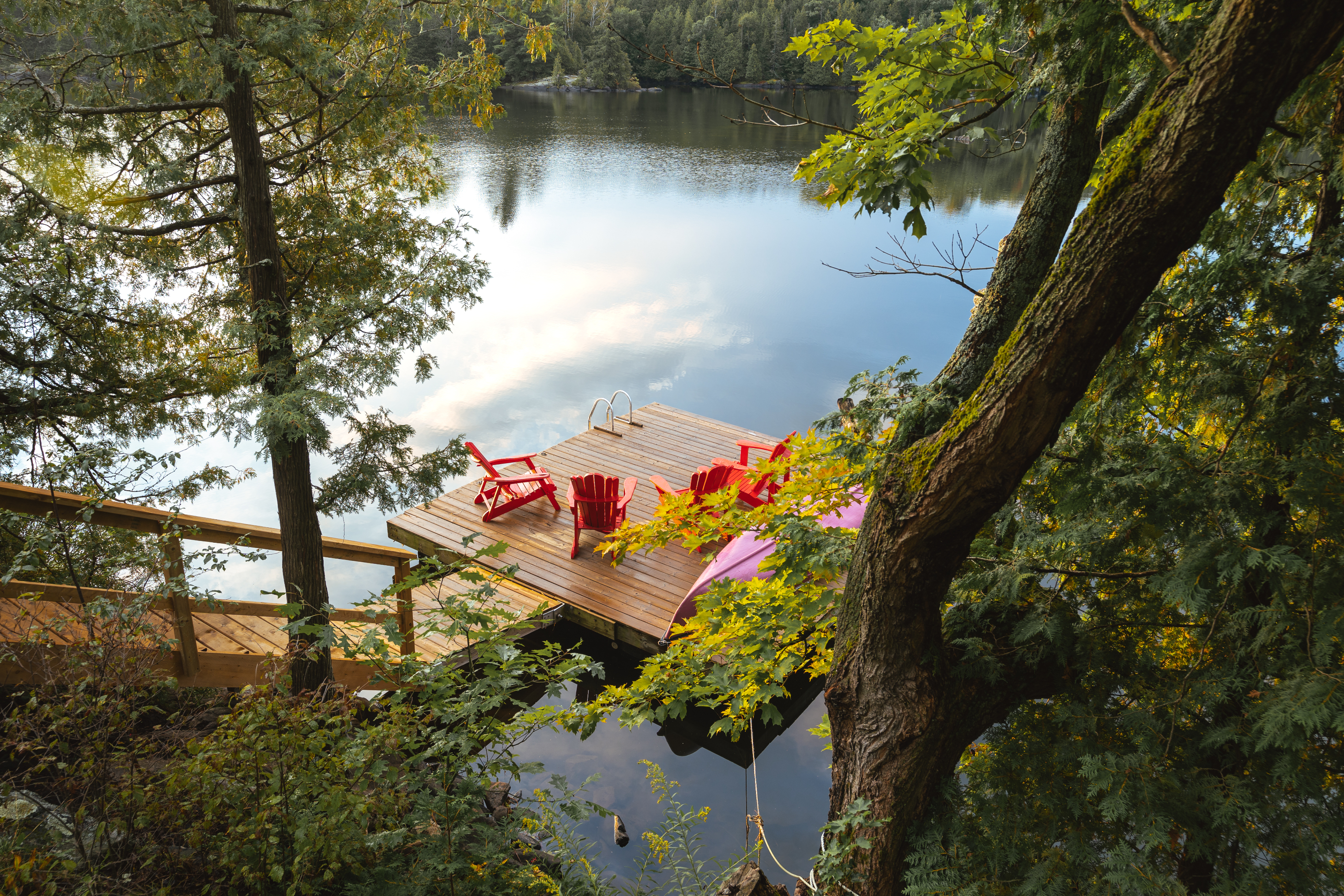 Wooden dock with two red chairs overlooking a calm lake, surrounded by greenery, no persons visible