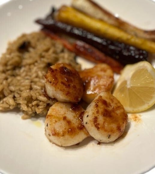 Plate with seared scallops, rice, roasted carrots, and a lemon wedge