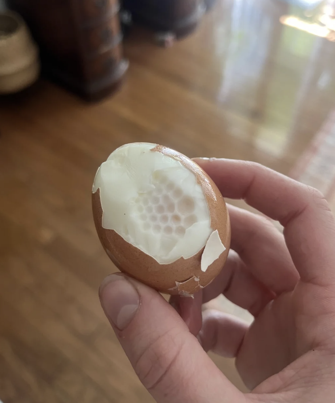 Person holding a partially peeled boiled egg with an unusual pattern on the white