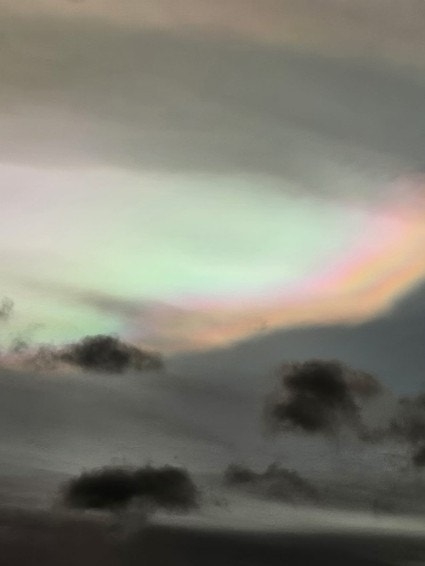 A blurry scene with a faint rainbow above silhouetted trees