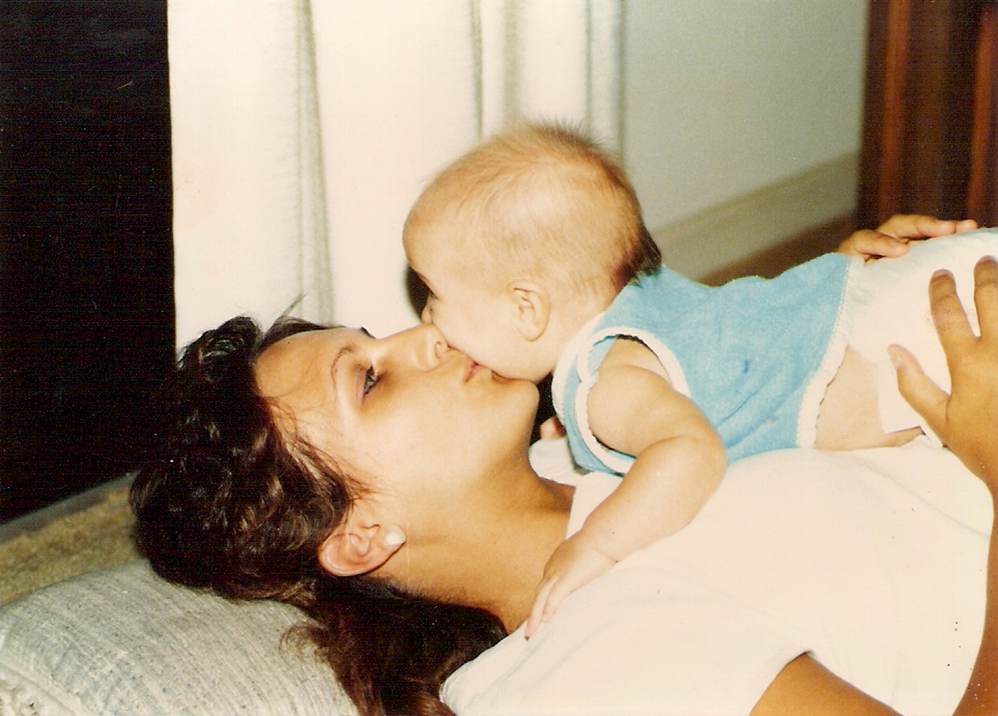 Woman lying down holding a baby up to her face, baby appears to be kissing her on the nose