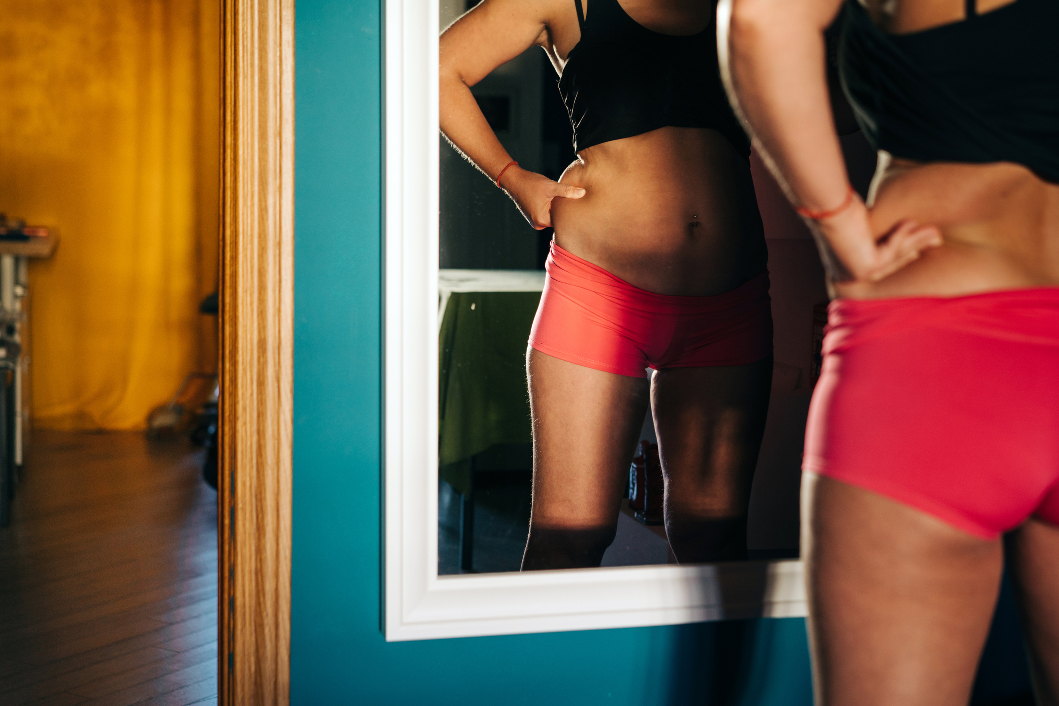 A person standing reflected in a mirror, showing only their torsos and legs