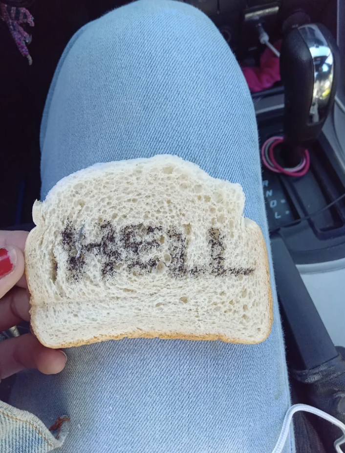 Someone holding a slice of bread with &quot;HELL&quot; written on it