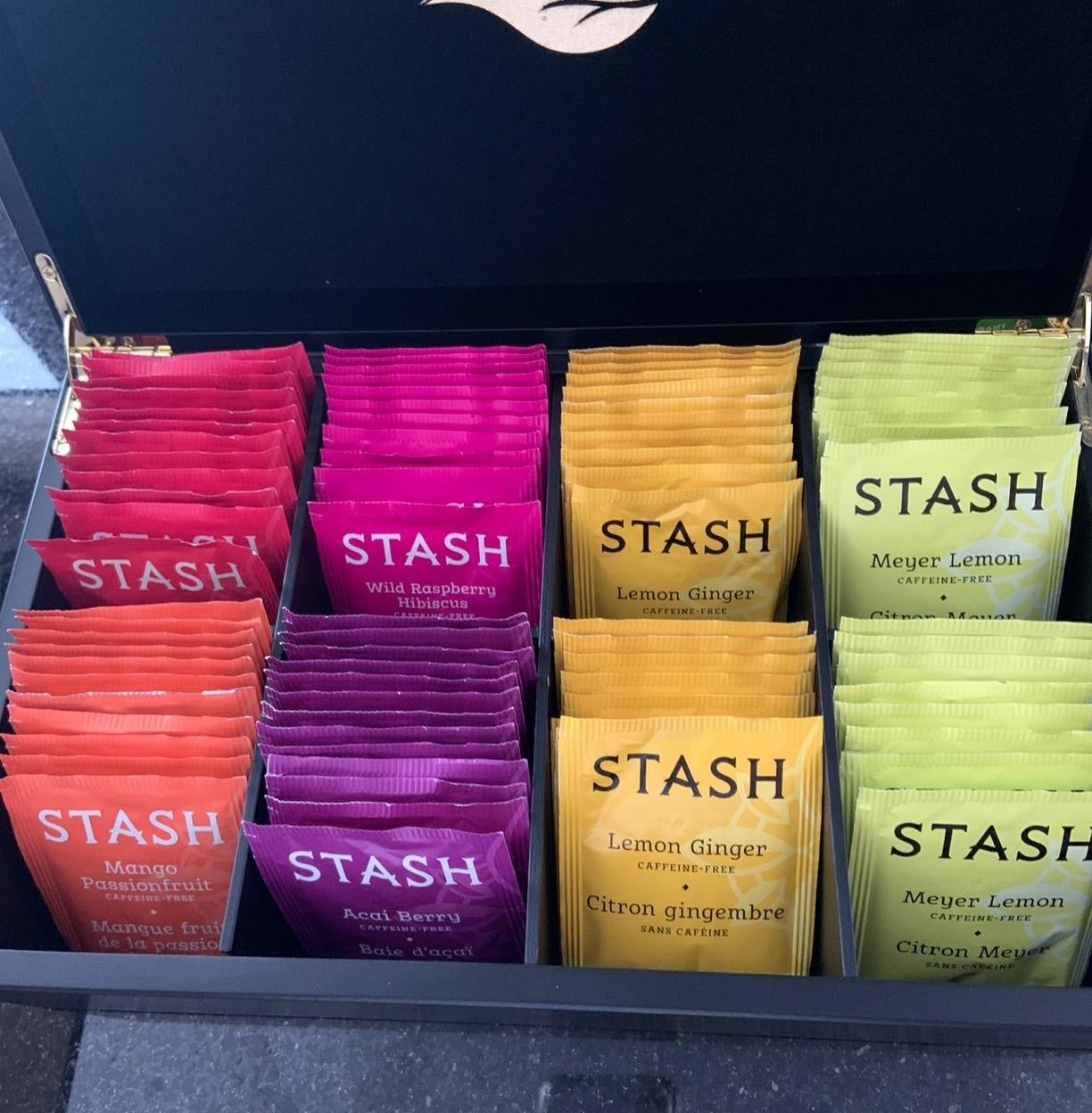 A variety of Stash tea packets, including Wild Raspberry, Lemon Ginger, and Meyer Lemon, are neatly organized in a box