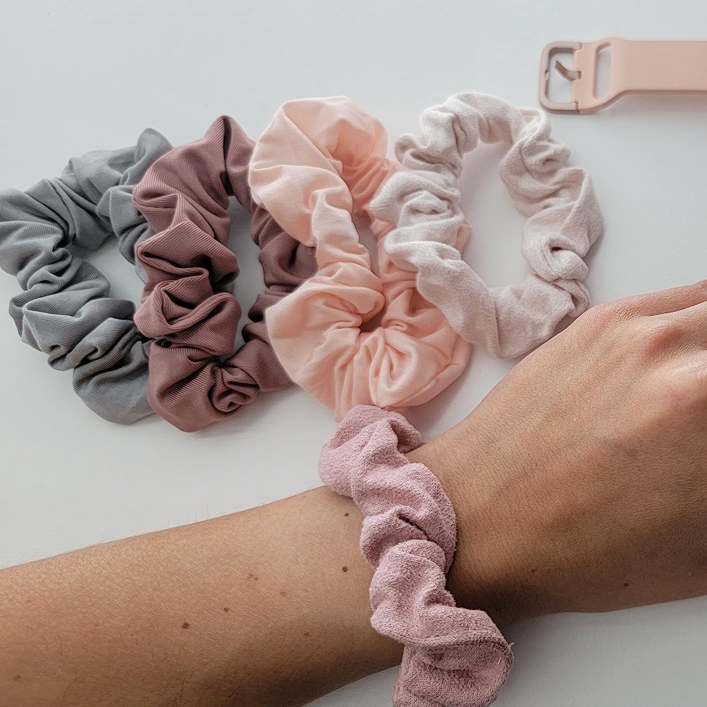 Four fabric hair scrunchies and a reviewer&#x27;s wrist wearing a scrunchie
