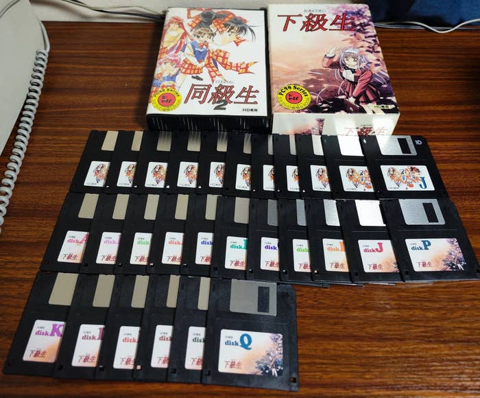 机の上にあるアニメキャラクターが描かれた複数のフロッピーとマンガ本。