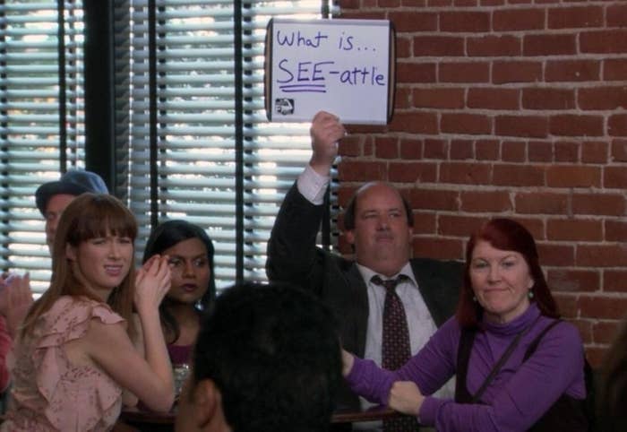 Group of people participating in a quiz, with a man raising a sign with a pun written on it