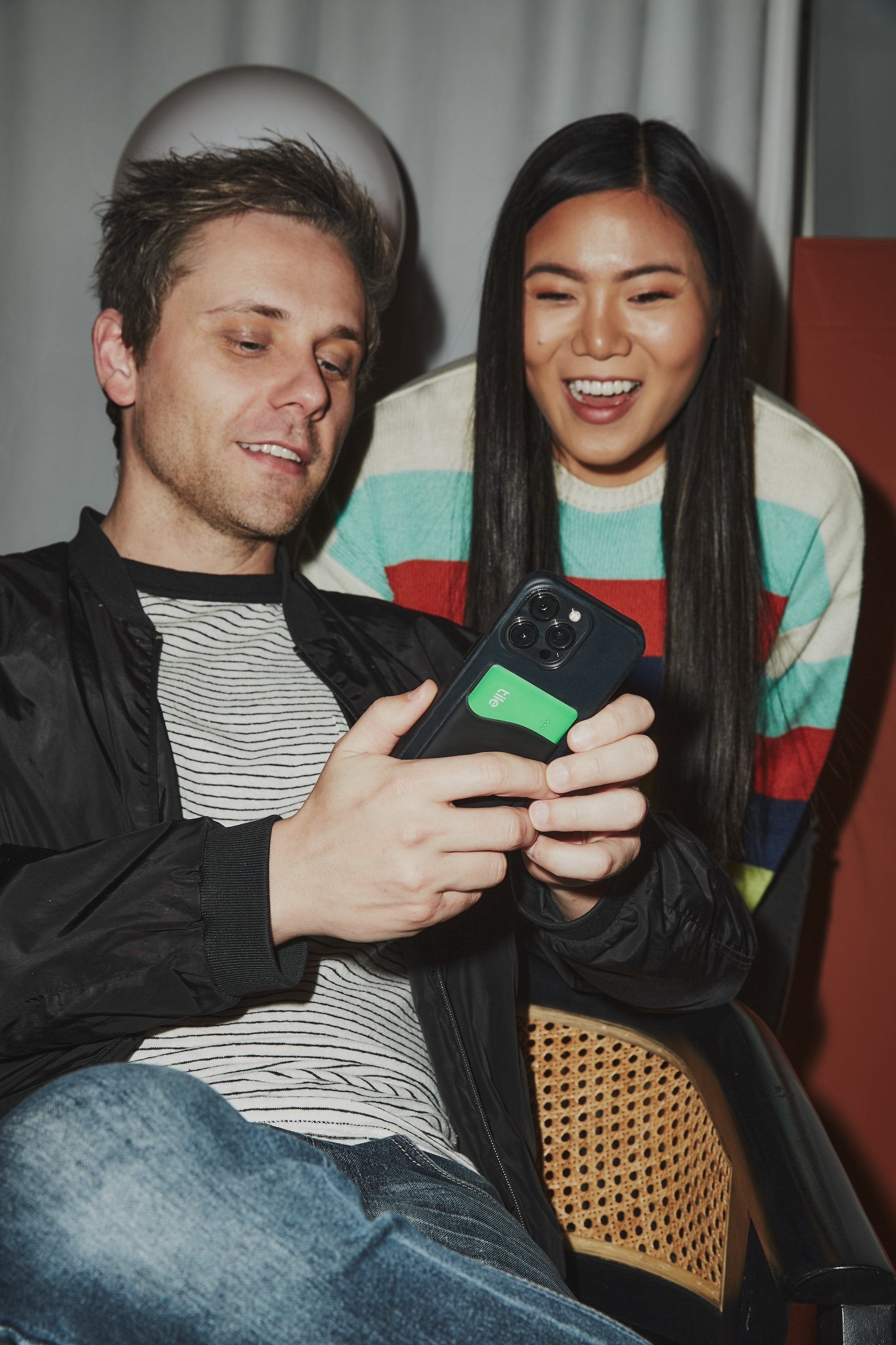 Man and woman smiling while looking at a smartphone he&#x27;s holding; the woman wears a striped sweater