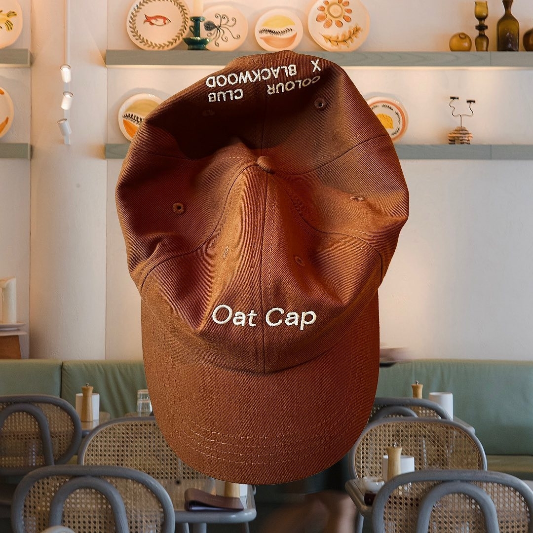 Embroidered &#x27;Oat Cap&#x27; in stylish font on a brown hat, displayed indoors with simple decor in the background