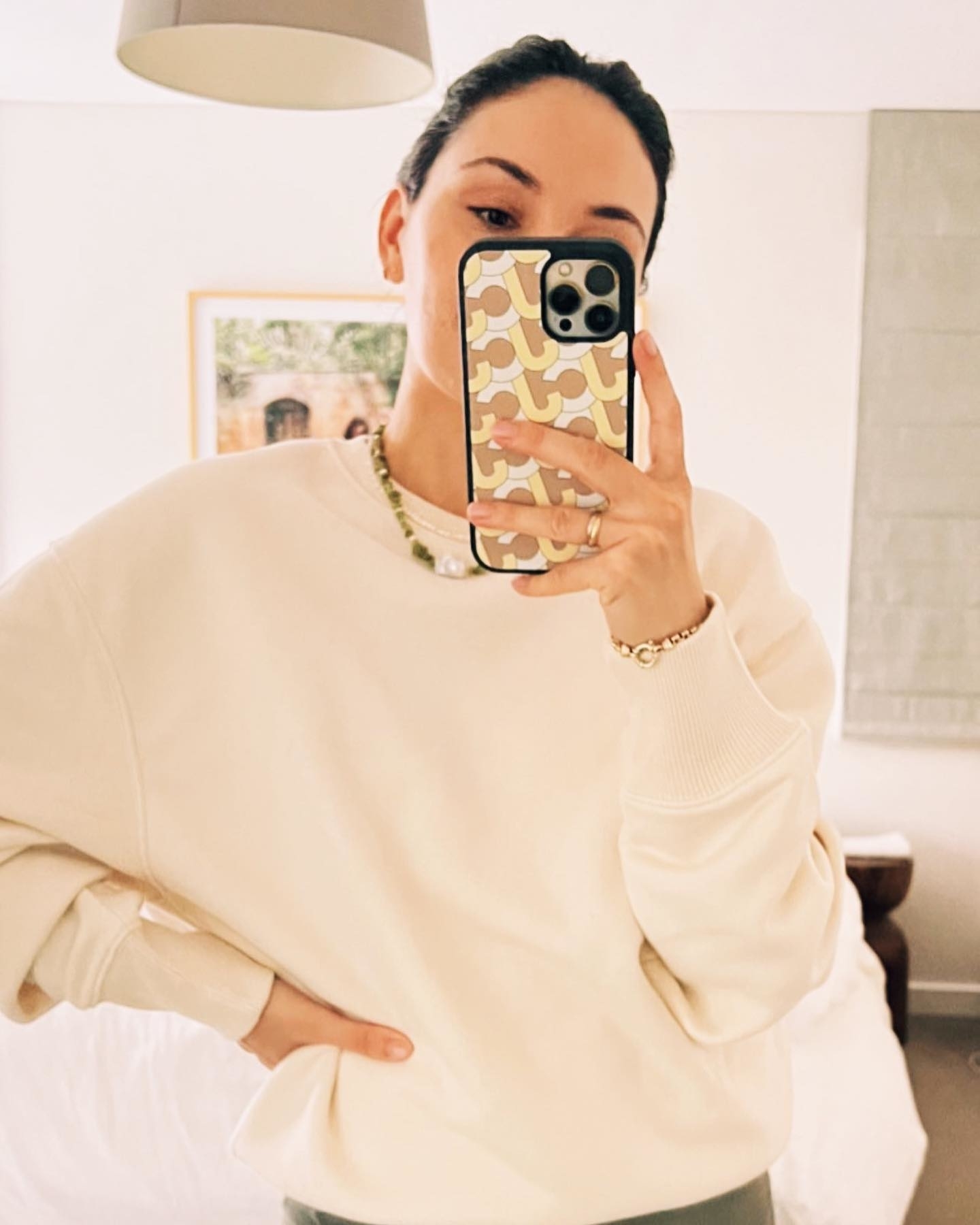 Person taking a selfie in a mirror, wearing a casual sweater and accessorized with a chunky necklace