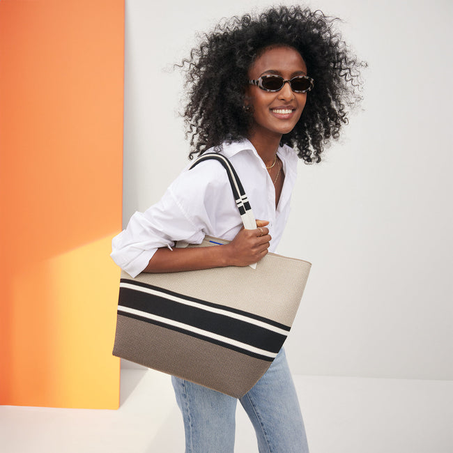 Woman modeling a white shirt and jeans with a striped tote bag, suitable for a shopping article