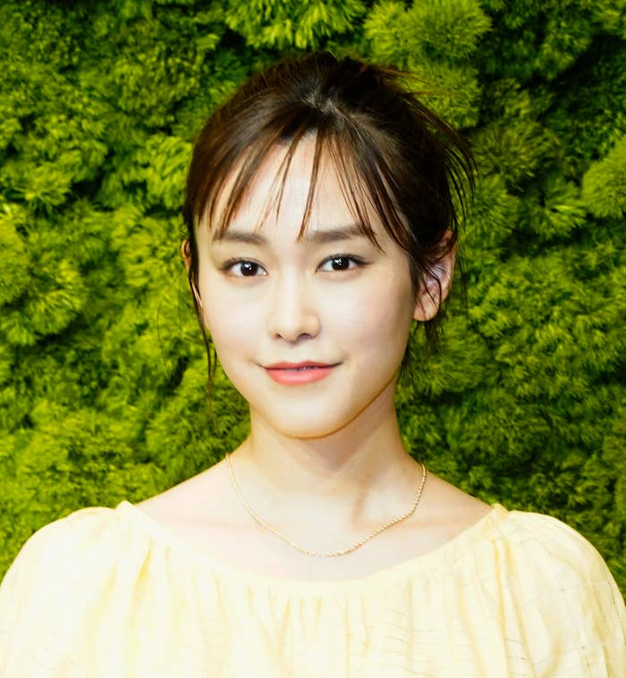 女性がカメラを見つめ、イエローのドレスを着ています。