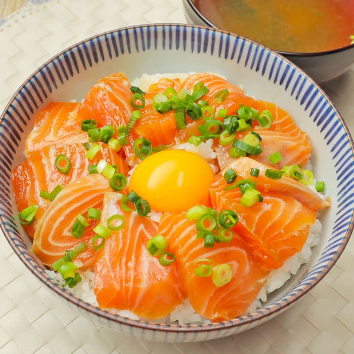 サーモンと生卵がのった丼と味噌汁が写っています。