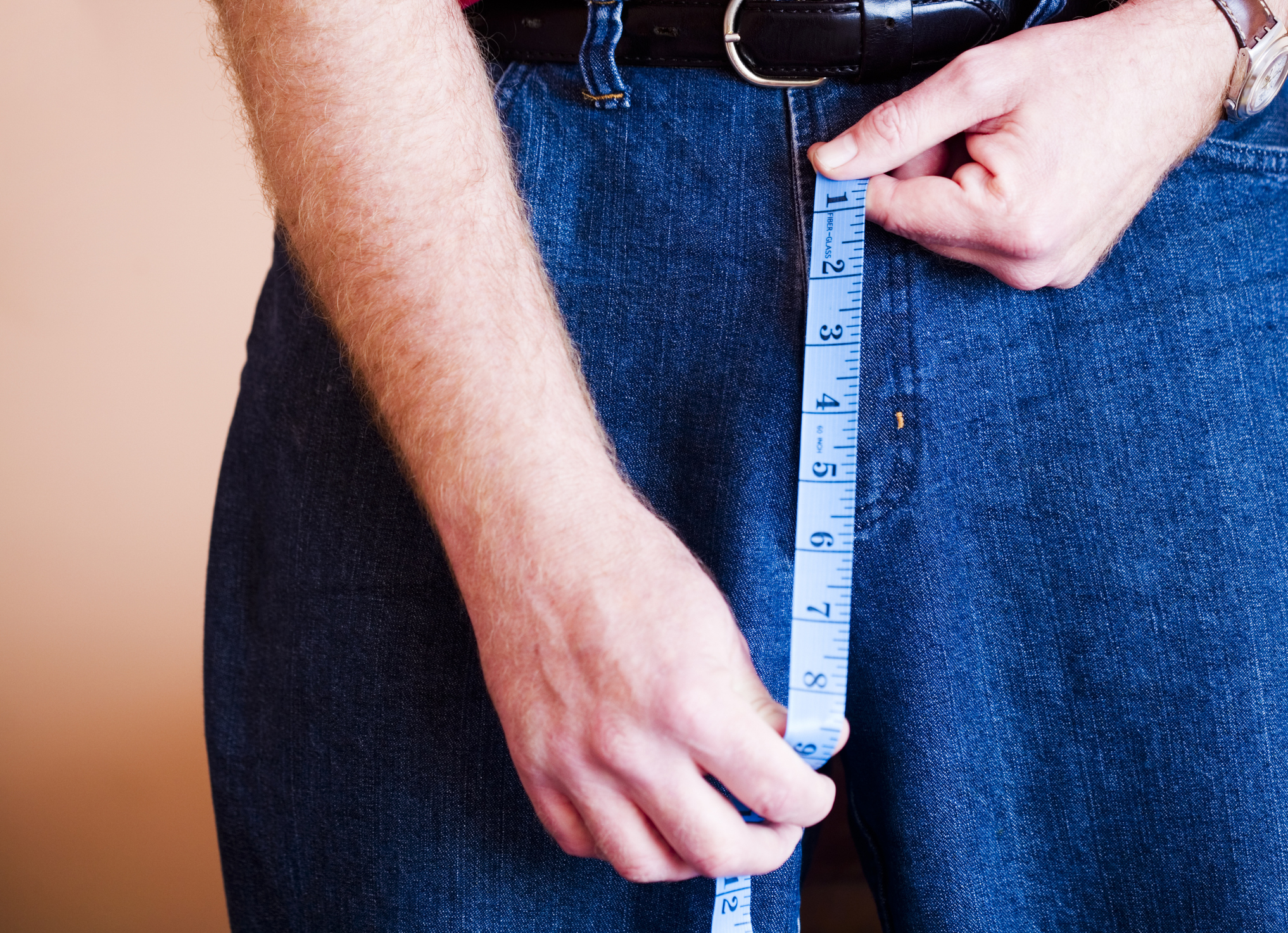Close-up of a person measuring waistline with a tape measure over jeans